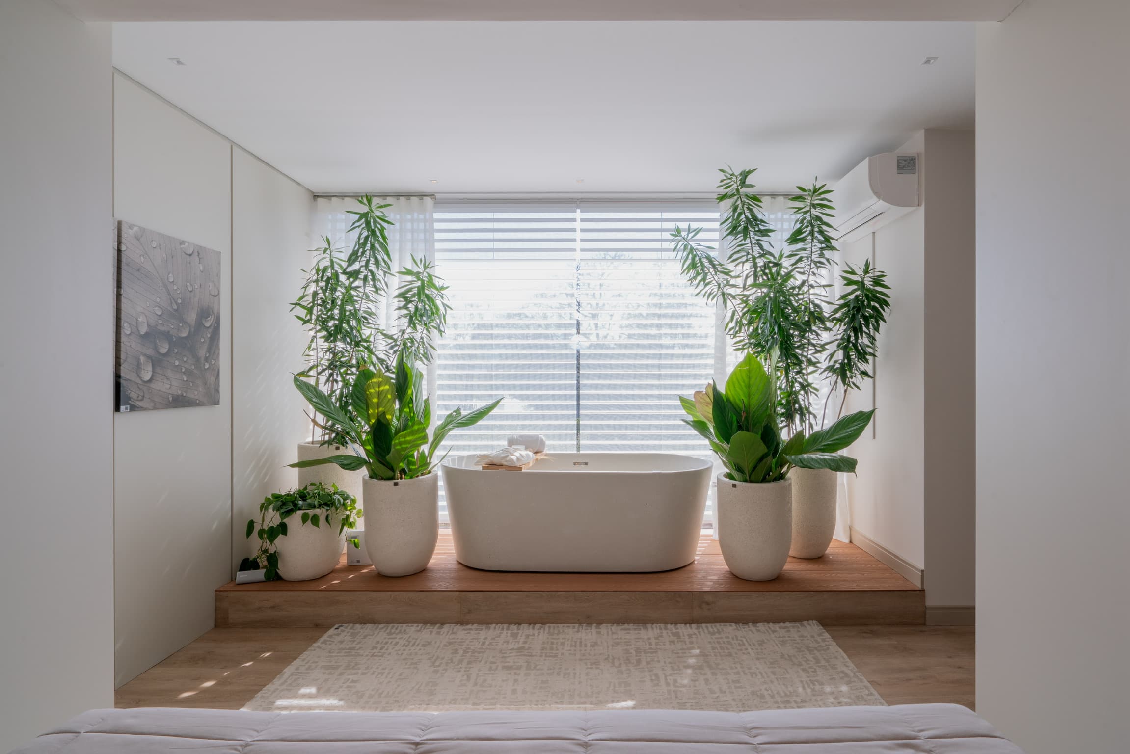 Banheira de imersão sobre deck de madeira, diante de janela com cortina e persiana horizontal, cercada por plantas — projeto Adriana Luz Arquitetura